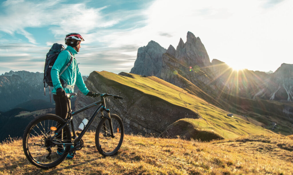 Young man with mountain bike cycling on Seceda mountain peak at sunrise in the Dolomites in Trentino