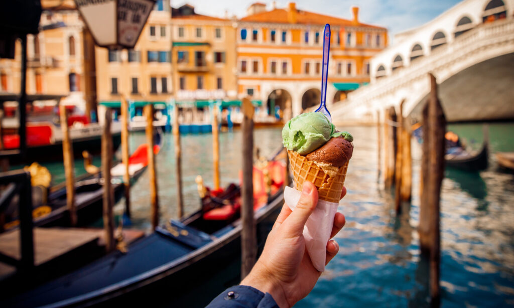 Hand man holds an Italian ice cream on background of Grand Canal and Handol in Venice, Italy. Concept tourism.