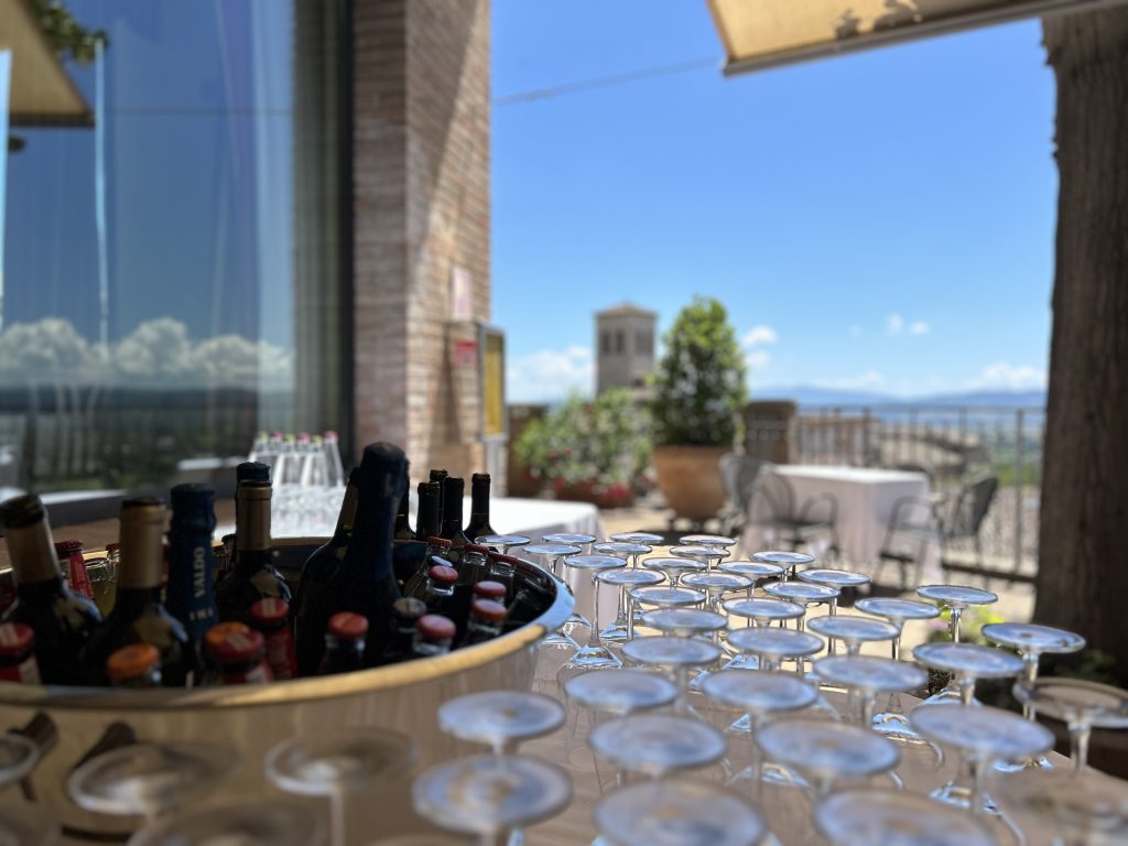 Table with glasses and wine on it, blue sky and sun.