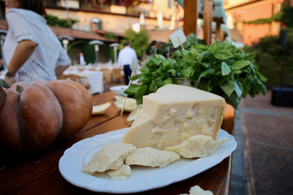 Piece of Parmesan cheese on a white plate, basil in the background.