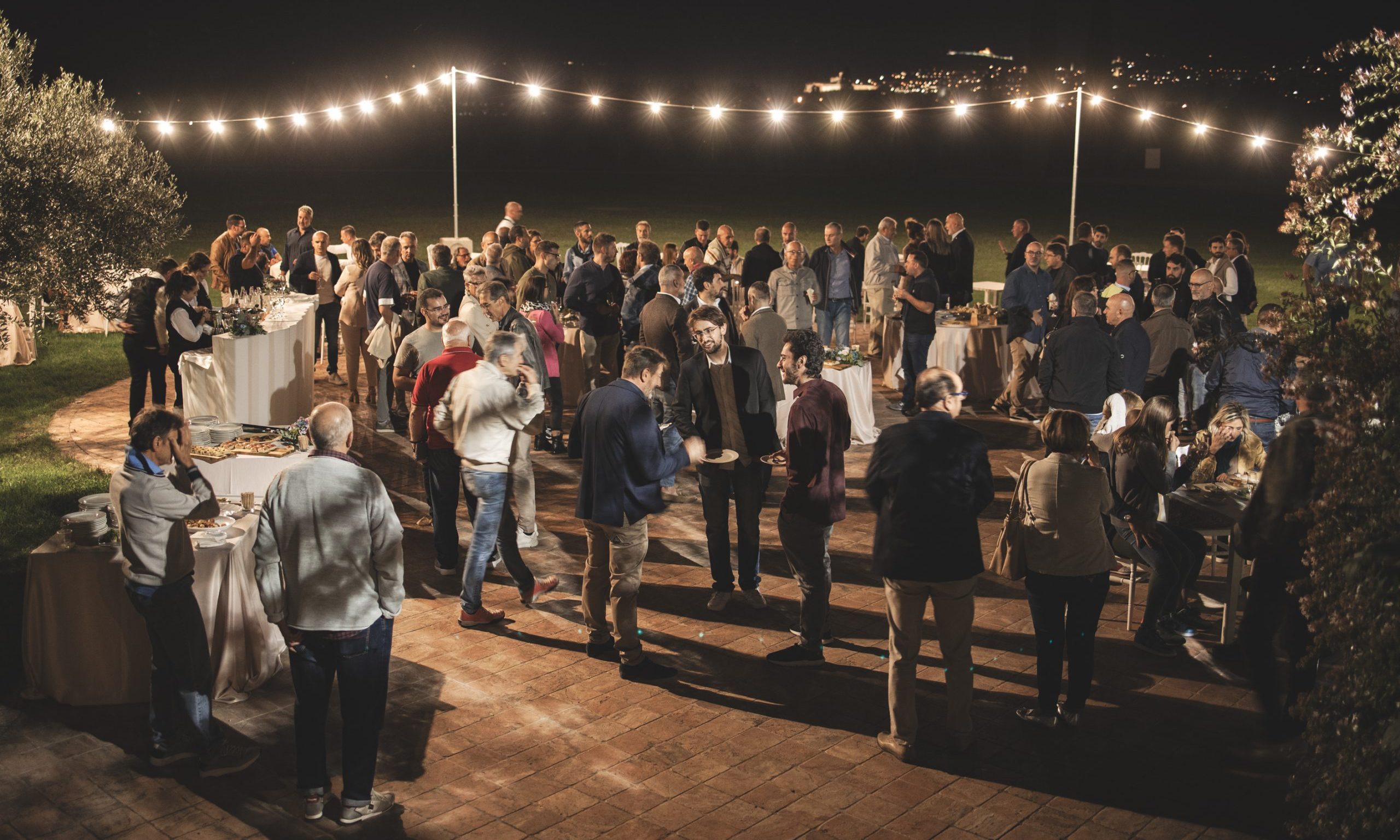 Group of people at a garden party outside at night, lights.