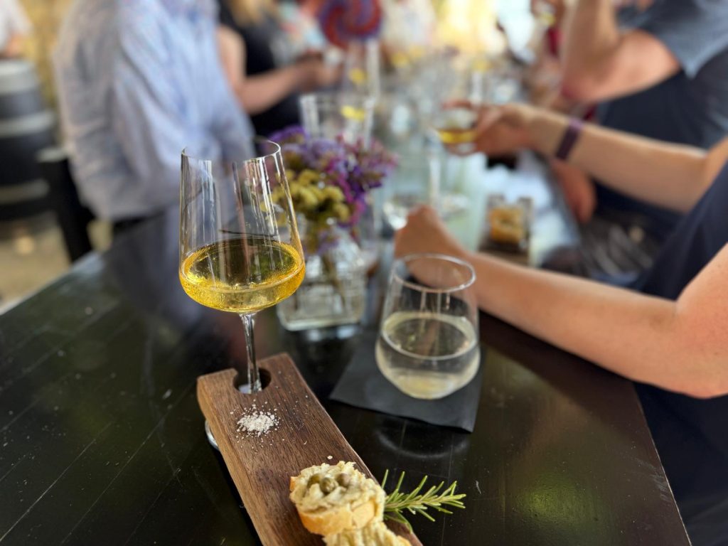 Wine Tasting, Table with a glas of white wine on it and a group of people sitting.
