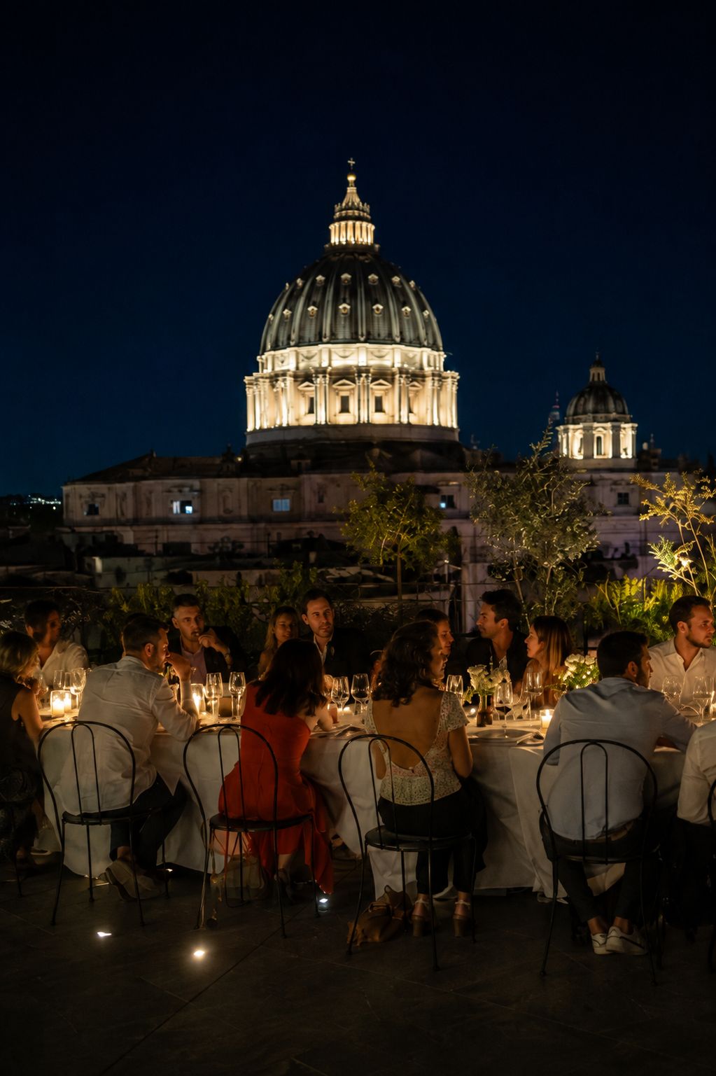 Eine Hotel-Dachterrasse im Zentrum von Rom, gedeckt für 16 Personen in der Abenddämmerung.