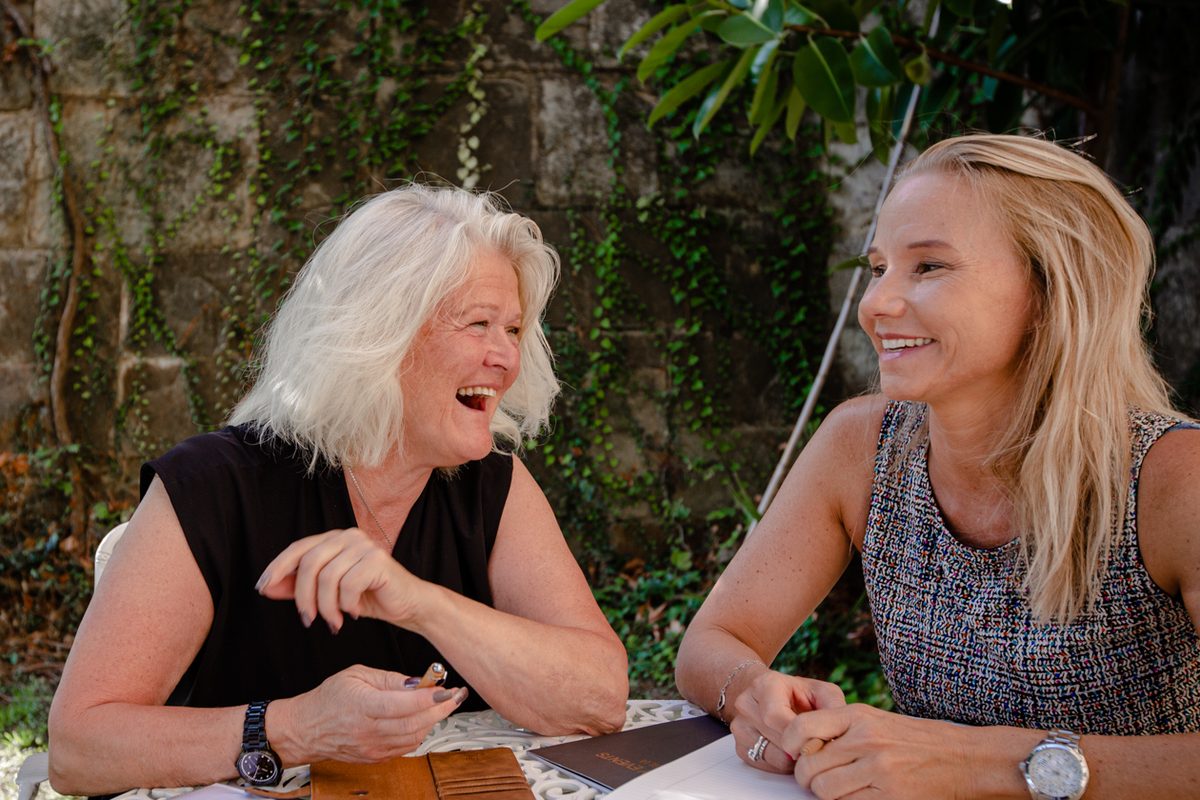 Christine lacht mit einer Kundin an einem Gartentisch bei der Planung eines Events