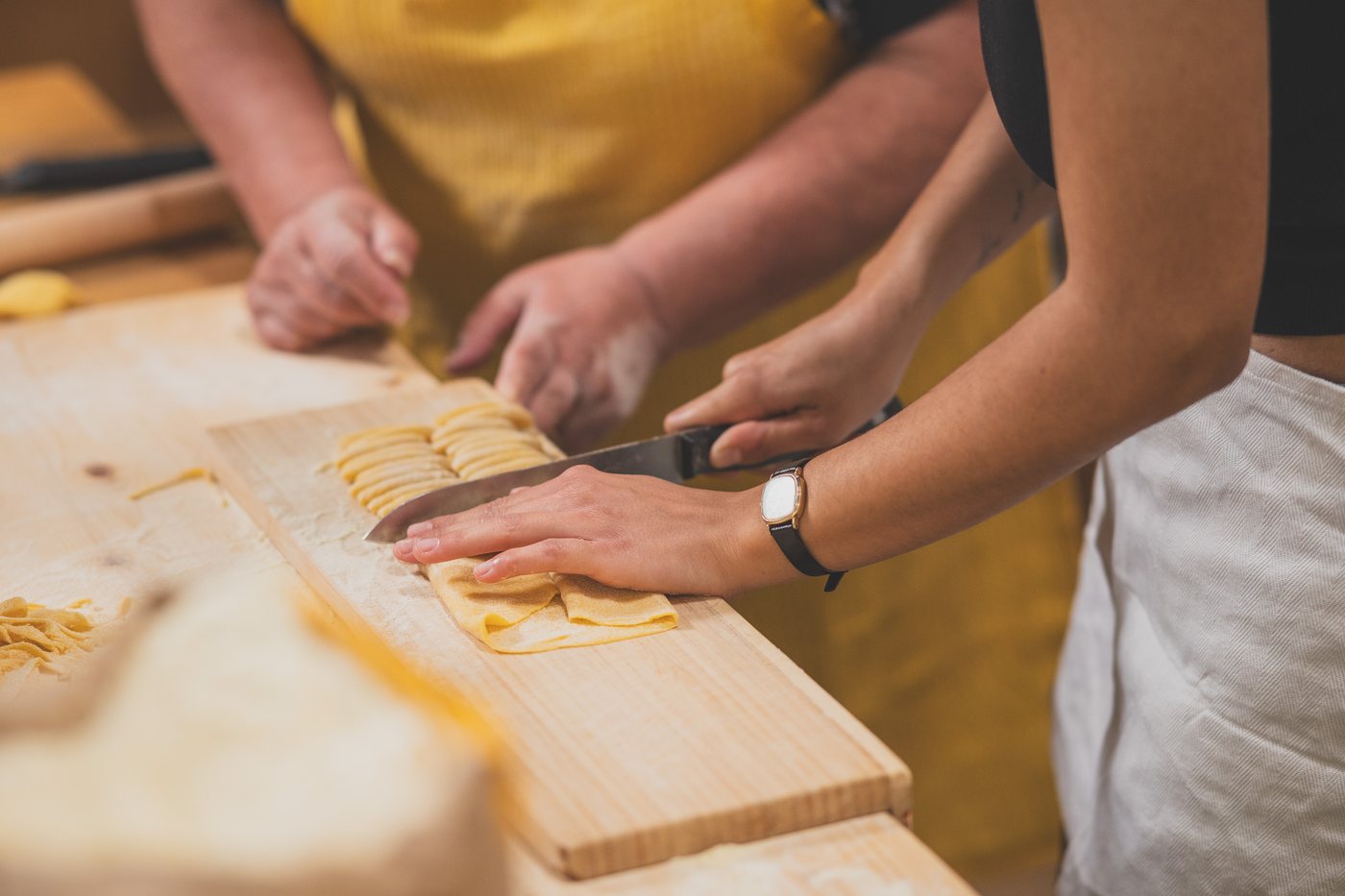 Hände schneiden frische Pasta auf einem Holzbrett bei einem Kochkurs in Rom