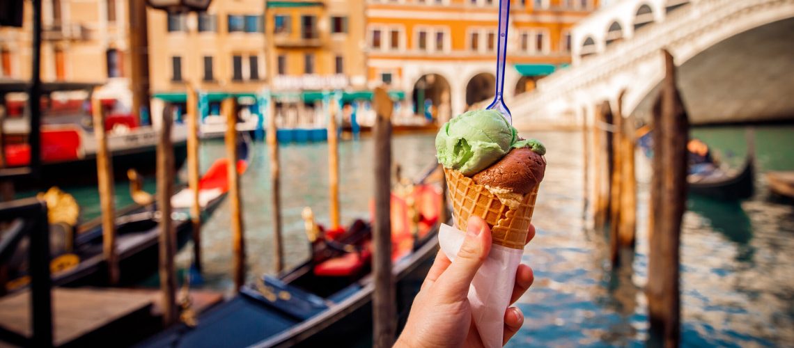Hand man holds an Italian ice cream on background of Grand Canal and Handol in Venice, Italy. Concept tourism.
