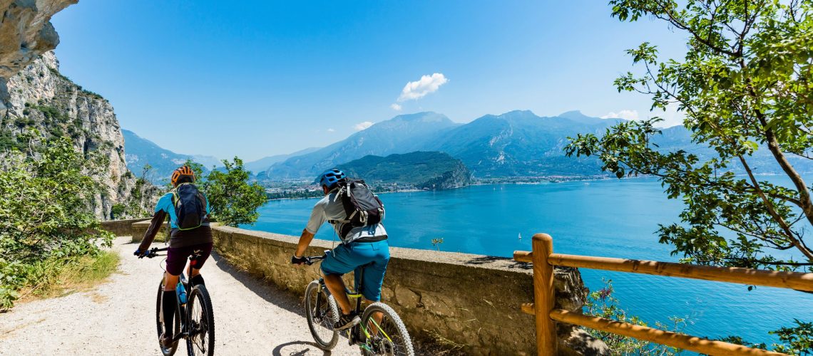Cycling woman and man riding on bikes at sunrise mountains and Garda lake landscape. Outdoor sport activity.